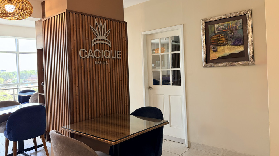 Restaurant tables at Cacique Hotel beside the wooden panel bearing the logo